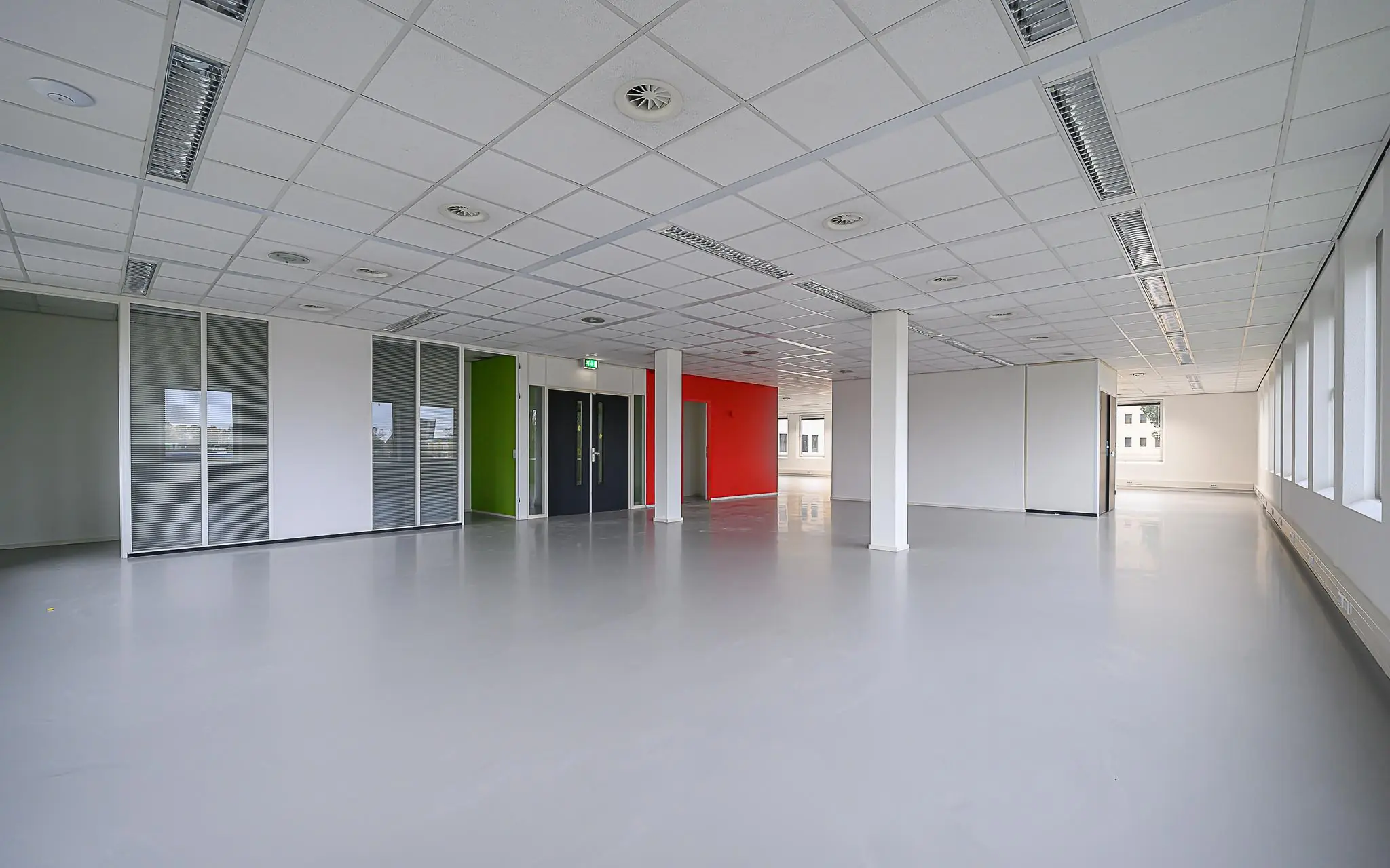 Leeg kantoorpand aan de Rivium Westlaan met witte wanden, een grijze vloer en glazen scheidingswanden.